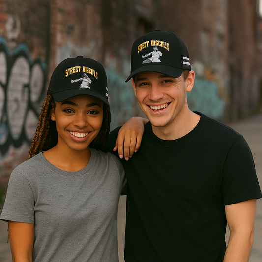 Two people wearing black caps with visible branding, standing outdoors against a graffiti-covered wall.